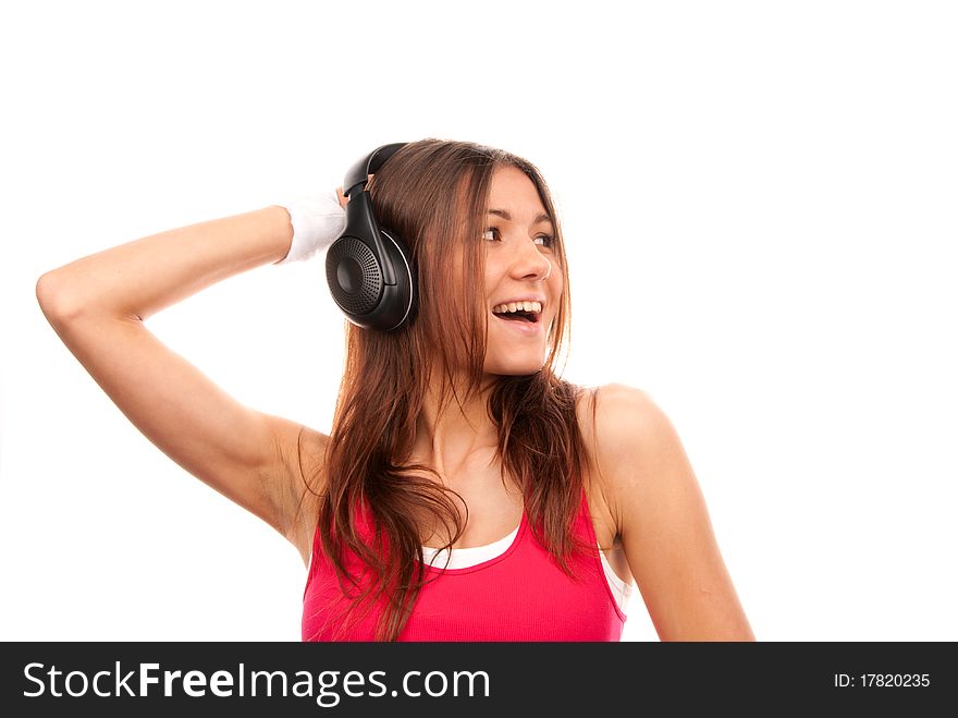 Girl listening music in headphones singing, smiling and holding her hand towards black headphones in pink top isolated on a white background