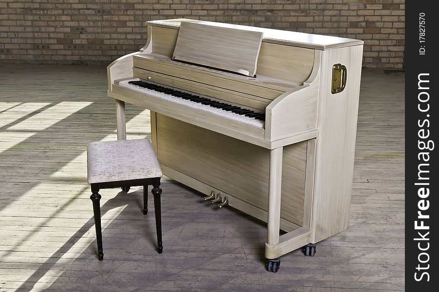 A blond finished upright piano in an old empty factory. A blond finished upright piano in an old empty factory