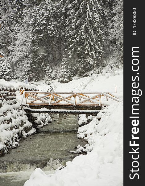 The bridge through the mountain river near wood, under going snow. The bridge through the mountain river near wood, under going snow