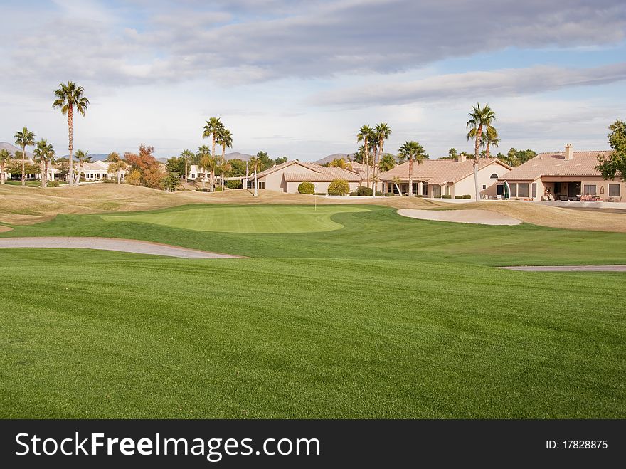 A golf course green on a cloudy day with palm trees and houses in the background. A golf course green on a cloudy day with palm trees and houses in the background.