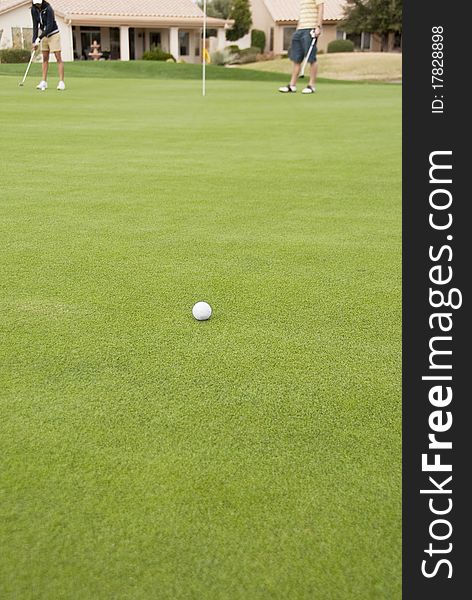 A golf ball on the green of a golf course with golfers in the background.