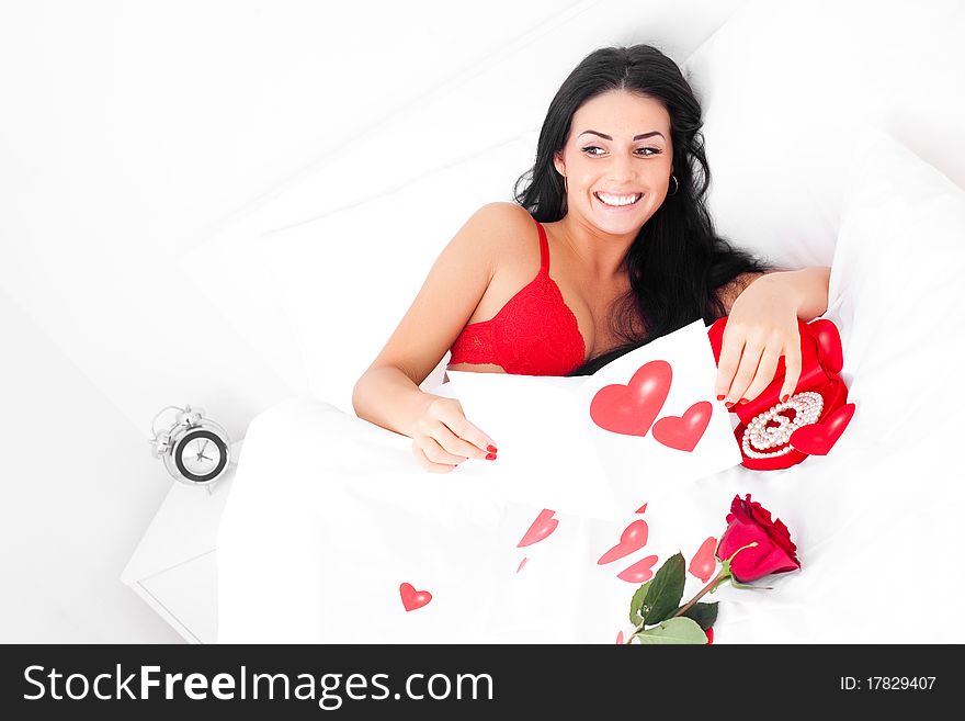 Beautiful brunette woman waking up at home on a Valentine's day with presents and a rose near her, prepared by her husband