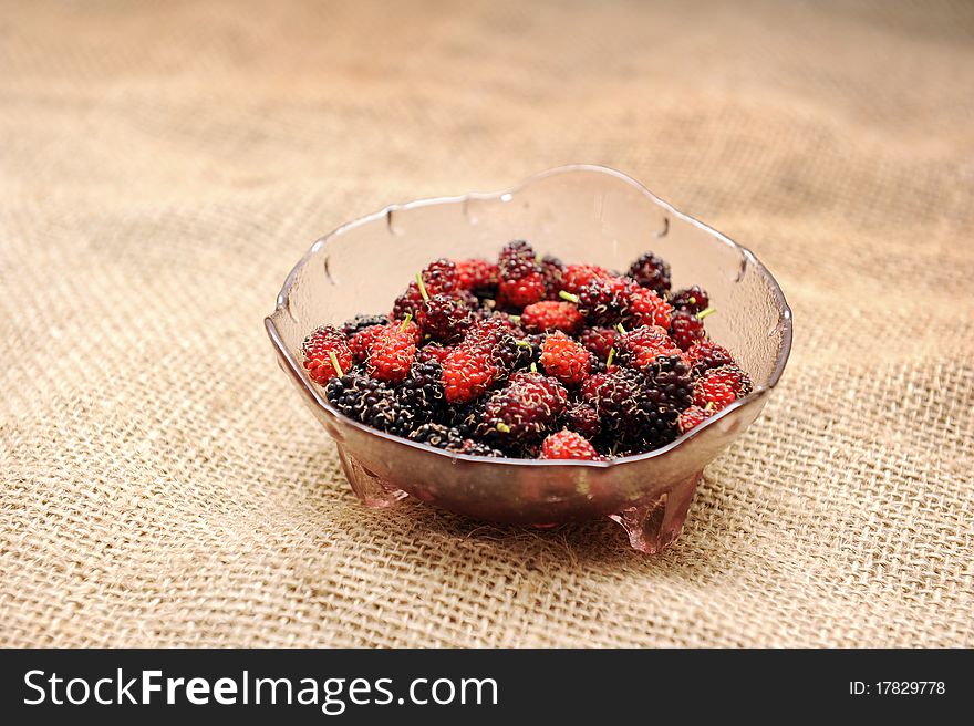 Close up of a bowl of fresh mulberry fruit on sack cloth.