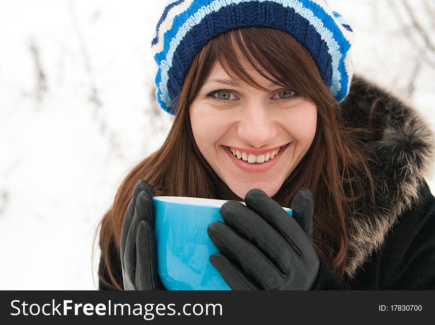 Beautiful girl in a striped beret laughing and holding a large blue mug. Beautiful girl in a striped beret laughing and holding a large blue mug