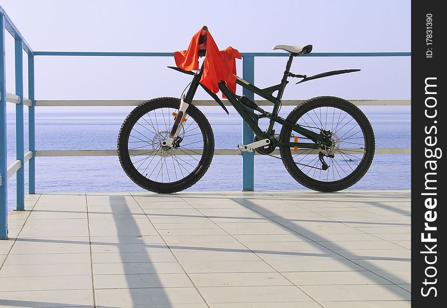 Alone bicycle at the seafront fence in sunny day against blue sea and sky