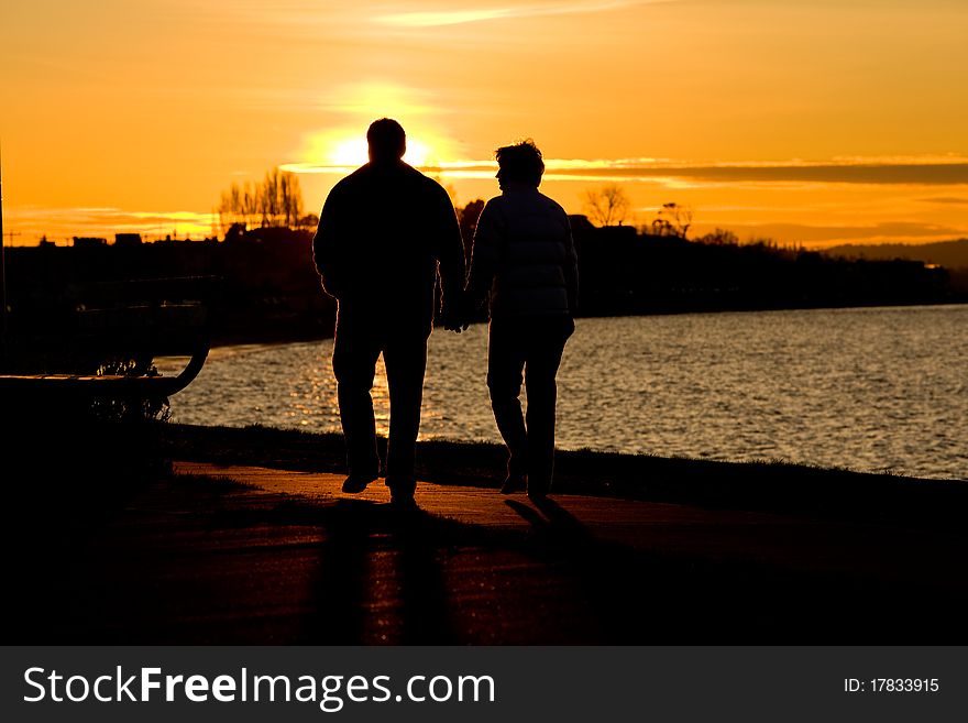 Couple Walking Along Waterfront At Sunset