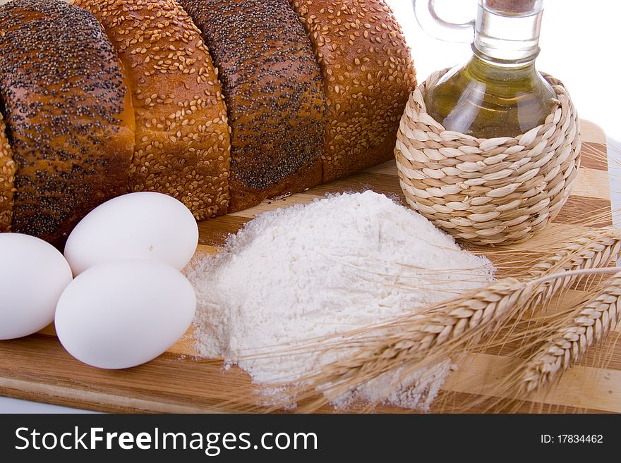 Fresh bread, eggs, flour and oil on wood board. Fresh bread, eggs, flour and oil on wood board