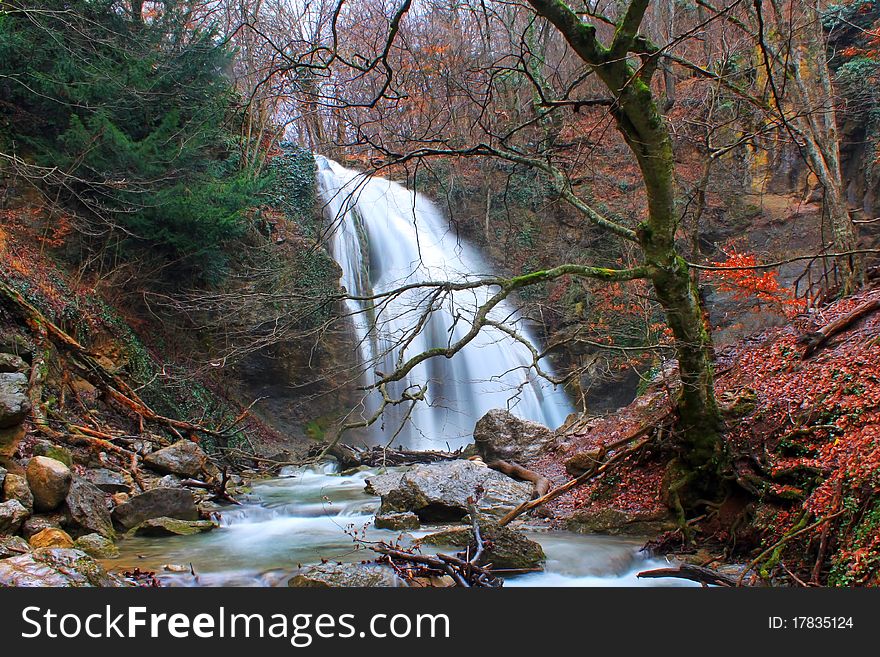 Trees in autumn colors around a waterfall with the flow of the cascading water smoothed by slow shutter speed. Trees in autumn colors around a waterfall with the flow of the cascading water smoothed by slow shutter speed.