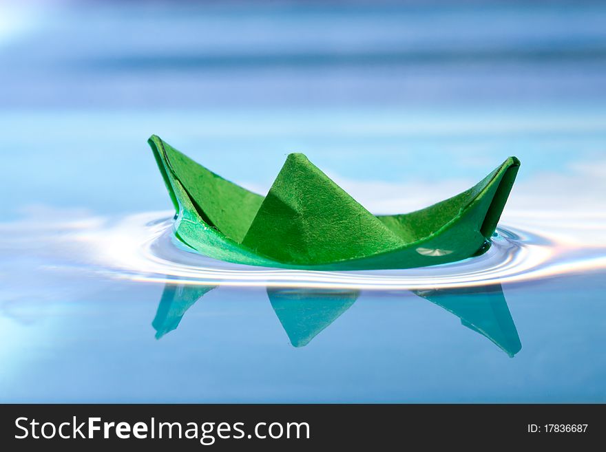 Green paper boat with reflection on blue water. Green paper boat with reflection on blue water