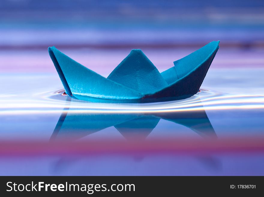 Blue paper boat and reflection on water, beautiful purple background