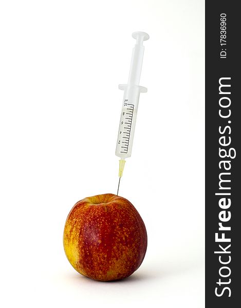 Syringe stuck into an apple on white background