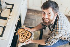 Bearded Young Man Taking Heart Shaped Cake Out Of The Oven Stock Photo