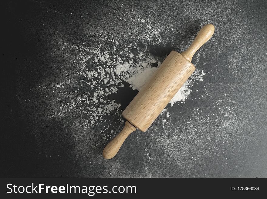 Wooden Dough Roller On The Black Table With Flour Spread