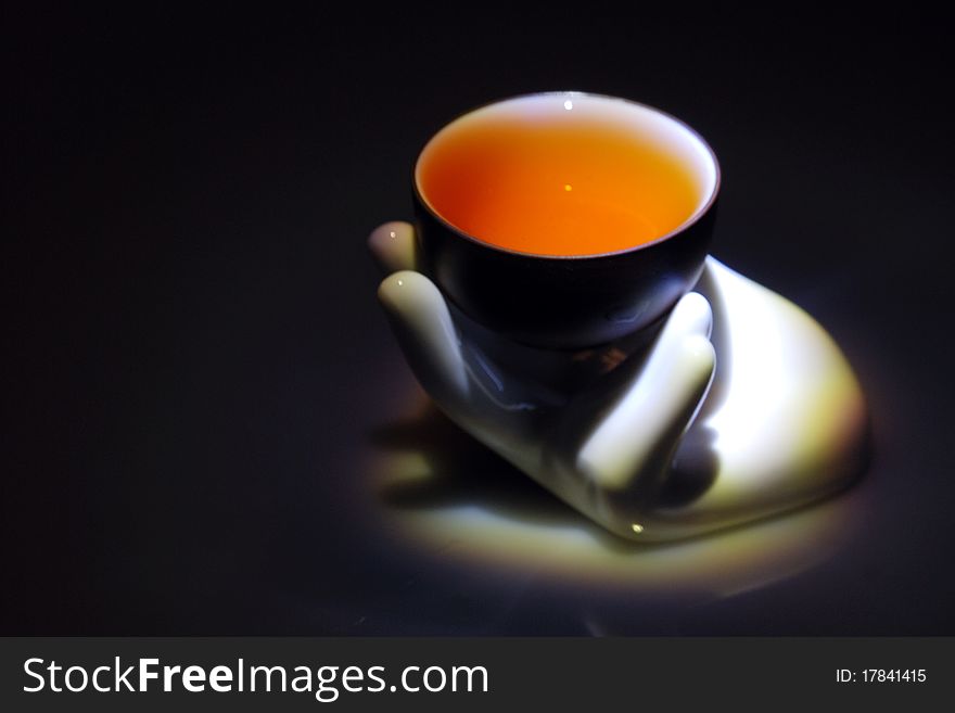 A teacup with tea on a hand-shape sculpture with black background.