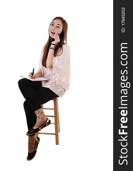 A young teenager sitting on a chair, in black tights and with long brunette hair and a notebook in her hand, on the cell phone, for white background. A young teenager sitting on a chair, in black tights and with long brunette hair and a notebook in her hand, on the cell phone, for white background.
