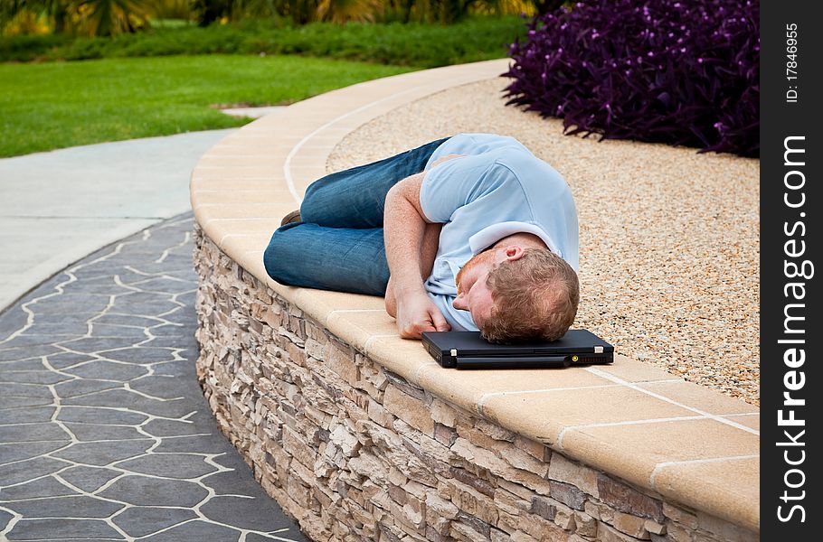 Man sleeping in a park with laptop as pillow