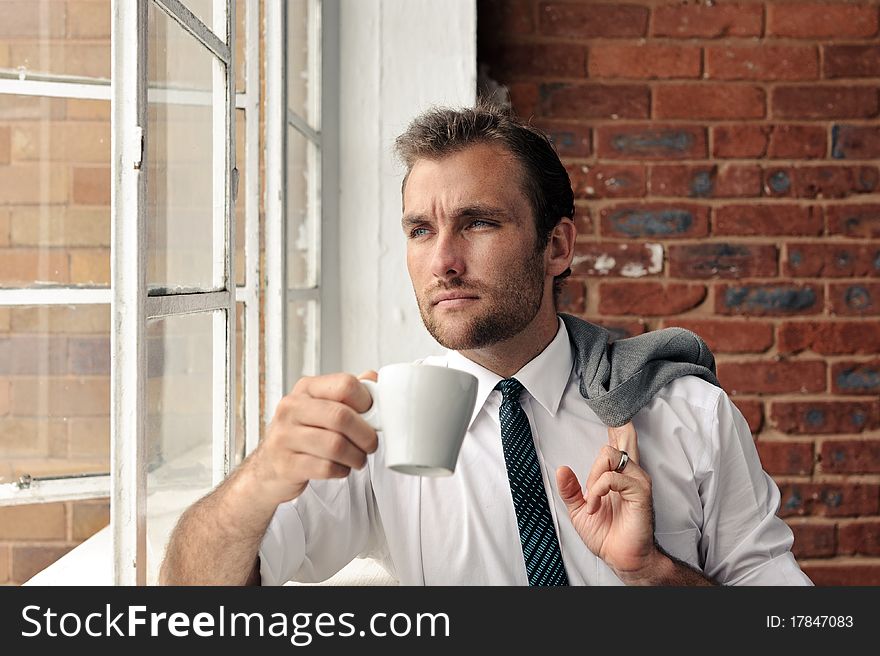 Young man stares out the window while holding a coffee cup. Young man stares out the window while holding a coffee cup