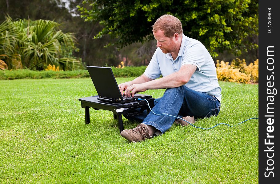 Man In Park Using Laptop With Ethernet Cable