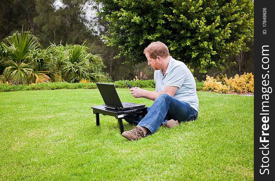 Man sitting in a park with a laptop and sending an SMS on his cell phone. Man sitting in a park with a laptop and sending an SMS on his cell phone.