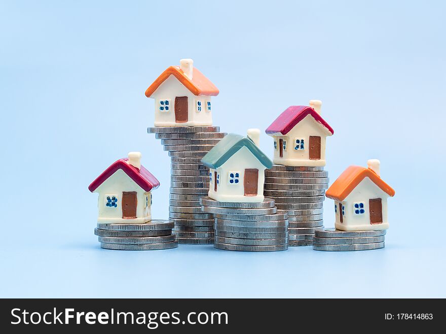 Mini house on stack of coins on a blue background. Concept of Investment property, Real estate, Saving money.