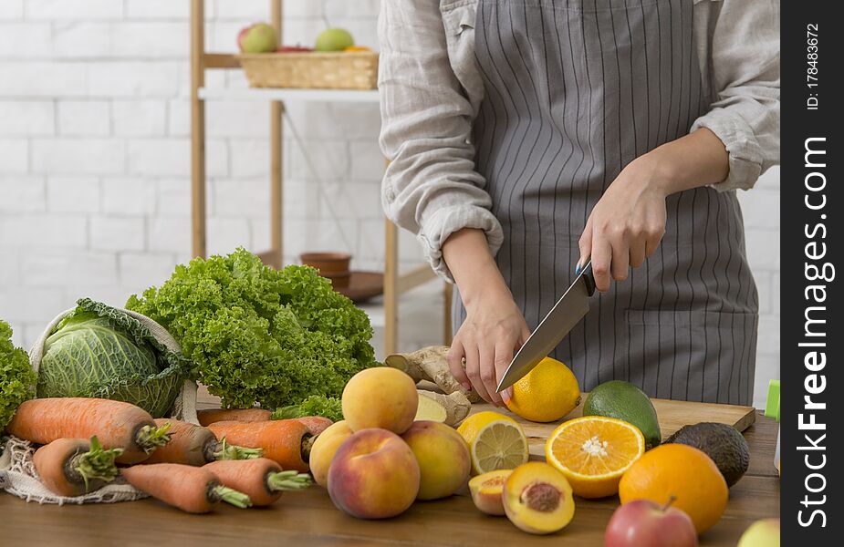 Vegan meal and detox concept. Unrecognizable woman cutting fresh fruits and vegetables for cooking smoothie, copy space