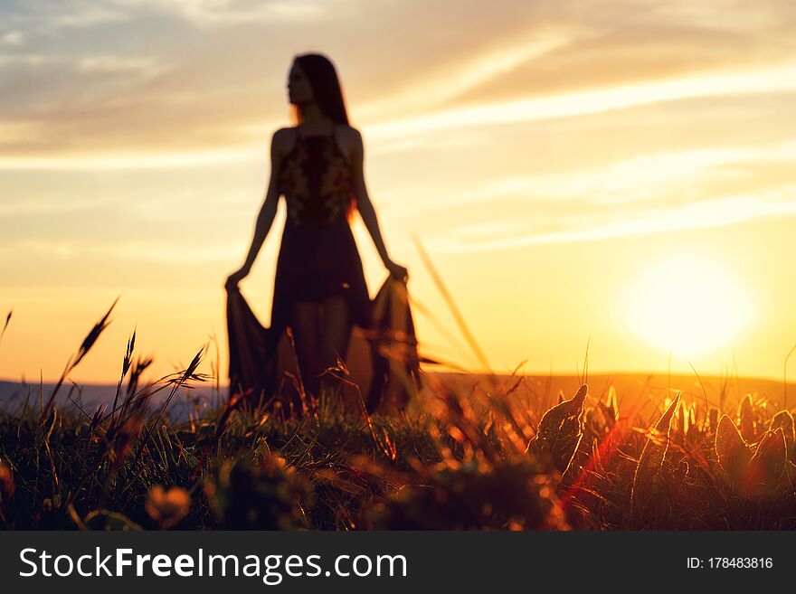 Young beautiful girl in a light summer dress posing in backlit sunset light standing barefoot on the grass. Young beautiful girl in a light summer dress posing in backlit sunset light standing barefoot on the grass