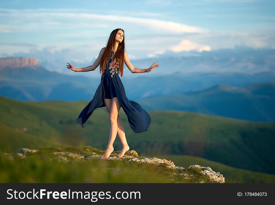 A young girl dancing on top of a mountain, against the backdrop of Caucasian ridge during sunset
