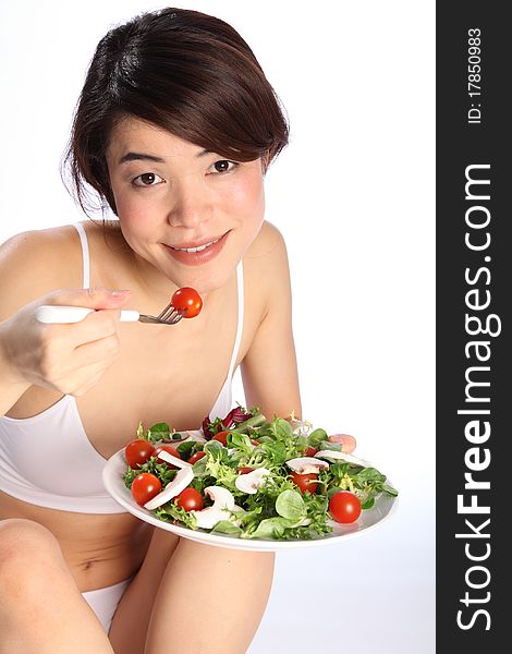 Beautiful, smiling young oriental girl, sitting on floor wearing sports underwear, showing off a healthy body while eating a salad. Beautiful, smiling young oriental girl, sitting on floor wearing sports underwear, showing off a healthy body while eating a salad.
