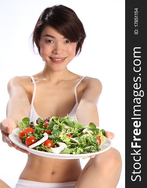 Beautiful, smiling young Japanese girl, wearing white sports bra, holds out a plate of green salad. Focus is sharp on salad with model out of focus in backdround. Beautiful, smiling young Japanese girl, wearing white sports bra, holds out a plate of green salad. Focus is sharp on salad with model out of focus in backdround.