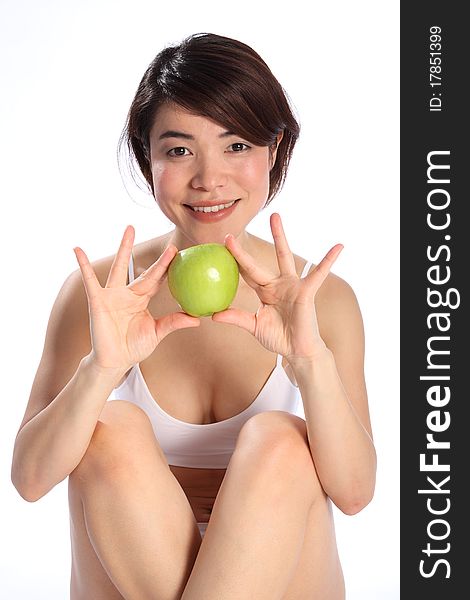 Beautiful young Japanese girl, wearing white sports underwear, sitting down holding a green apple. Beautiful young Japanese girl, wearing white sports underwear, sitting down holding a green apple.