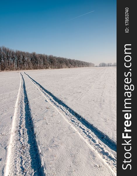 Landscape with a trace of the aircraft in the clear sky and a long snowy country road. Landscape with a trace of the aircraft in the clear sky and a long snowy country road