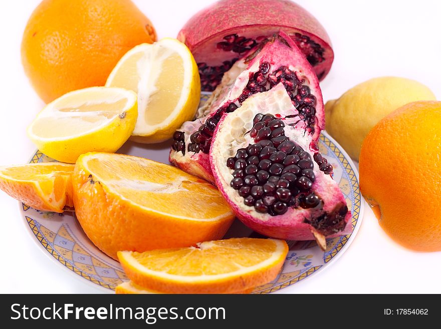 Cut pomegranate, orange and lemon on a plate isolated on white background. Cut pomegranate, orange and lemon on a plate isolated on white background