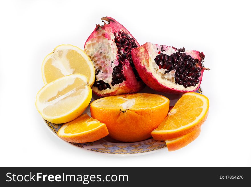 Cut pomegranate, orange and lemon on a plate isolated on white background. Cut pomegranate, orange and lemon on a plate isolated on white background