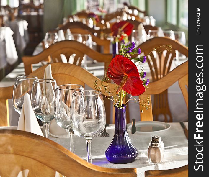 Table is set in a restaurant with glasses, flowers and tablecloth