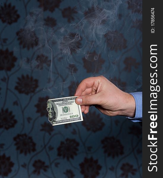 Smoking one hundred dollars bill in mens hand on dark background. Smoking one hundred dollars bill in mens hand on dark background