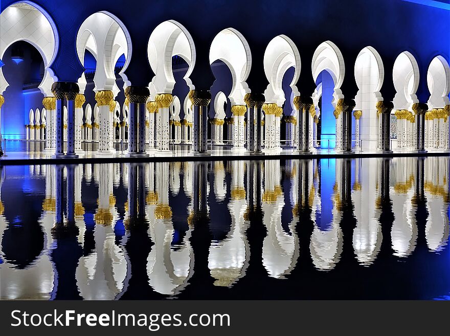 Beautiful white columns of the mosque are reflected in the water of the pool. Contrast of blue backlight and white columns. Beautiful white columns of the mosque are reflected in the water of the pool. Contrast of blue backlight and white columns.
