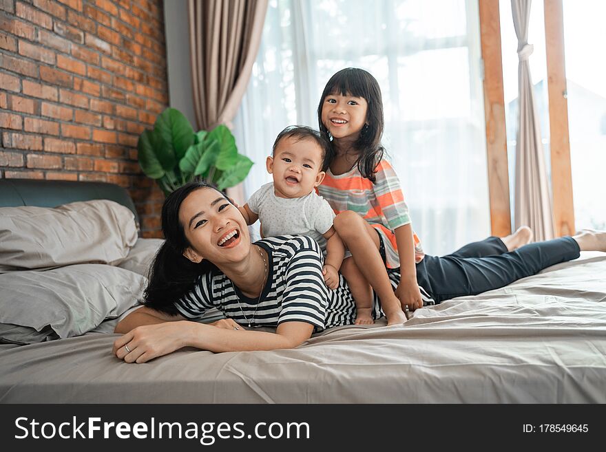 Happy children sitting on mother`s back playing piggyback ride at home
