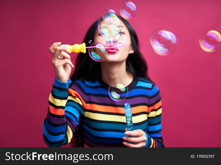 Happy beautiful woman blowing soap bubbles isolated over pink background