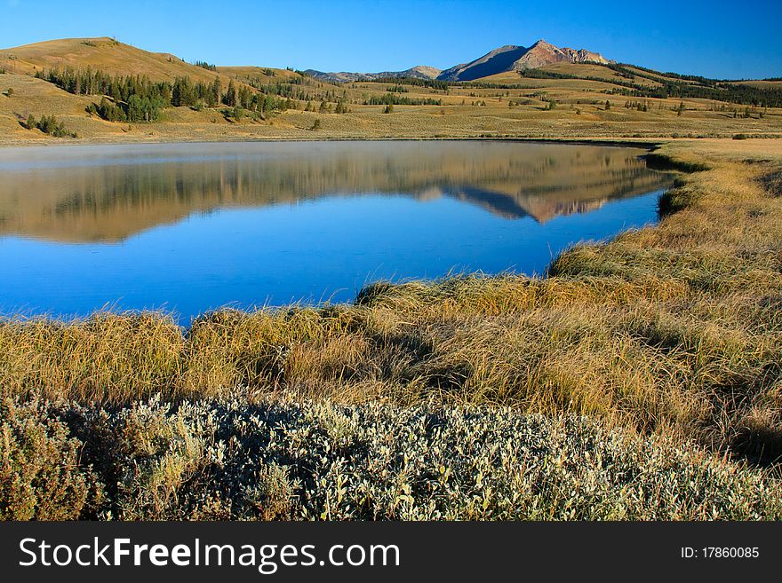 Steep mountain reflected in calm water of a blue lake surrounded by fall grass. Steep mountain reflected in calm water of a blue lake surrounded by fall grass.