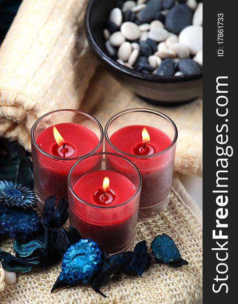 Three red candles and a bowl of black and white rocks on a towel