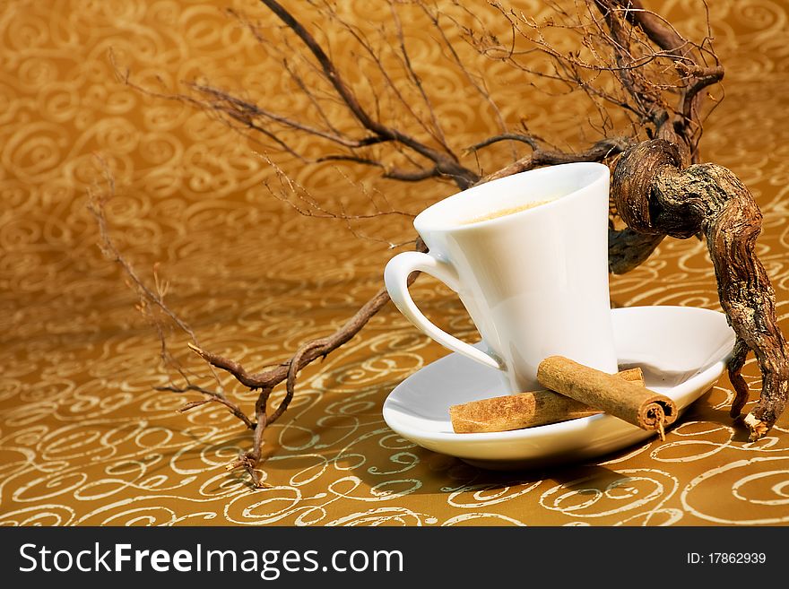 Cup of coffee with cinnamon sticks in the background with brown trunks