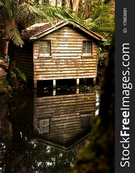 An old cabin and its reflection beside a pond in the middle of a forest.