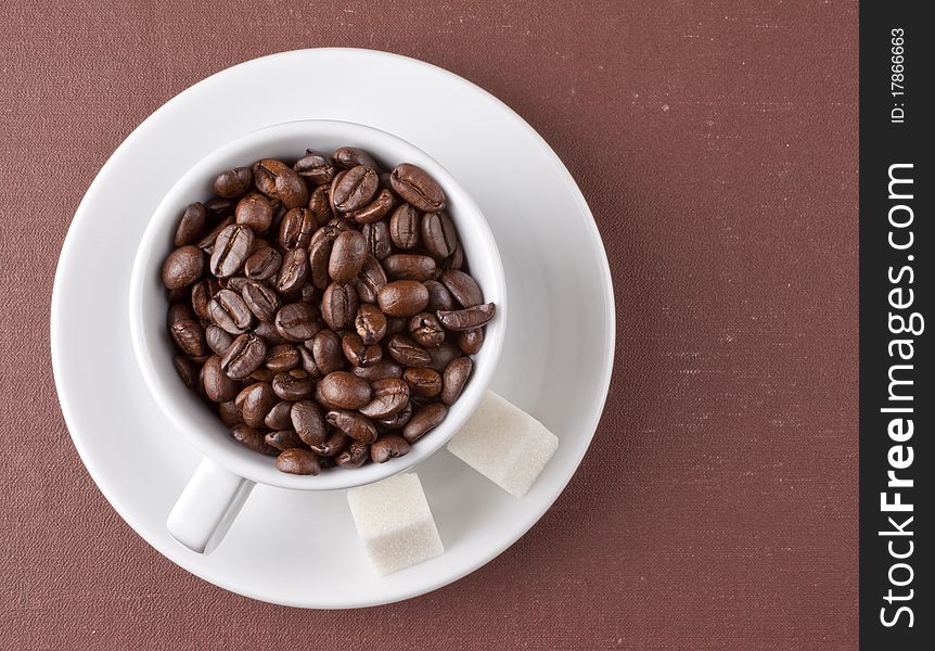 White cup with coffee grains on a brown background