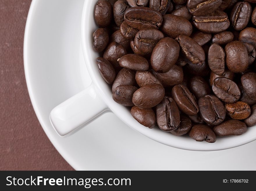 White cup with coffee grains on a brown background