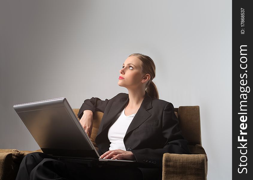 Businesswoman sitting on an armchair with a laptop on her knees and reflecting. Businesswoman sitting on an armchair with a laptop on her knees and reflecting