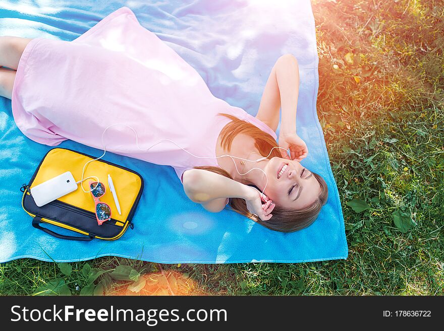 Online media entertainment. Music streaming. Top view of pretty woman relaxing on grass in park listening to music.