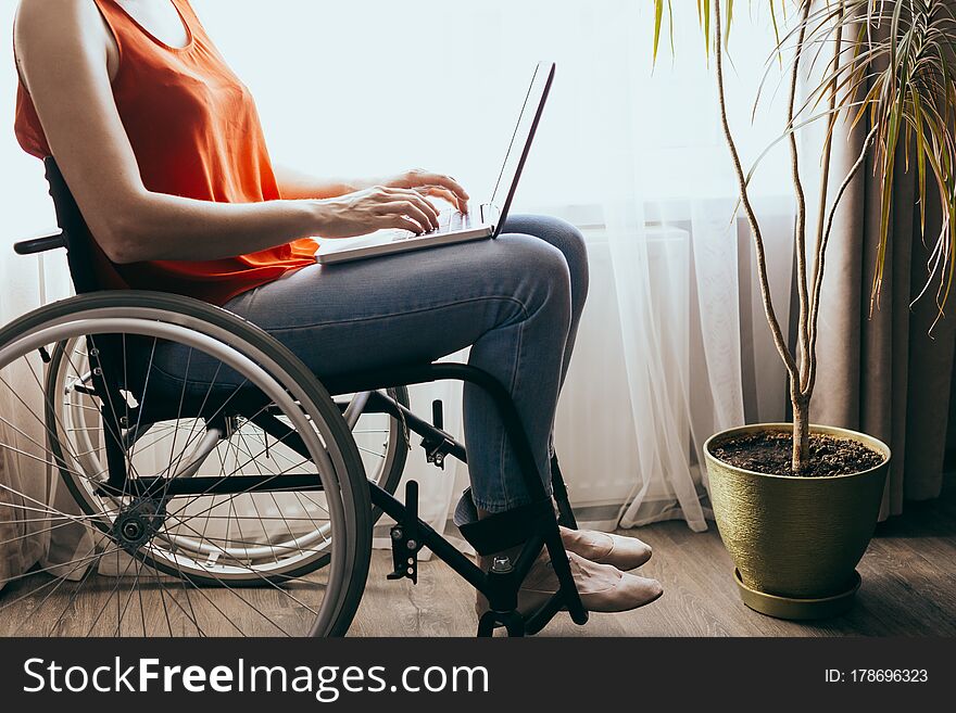 Woman in a wheelchair at home with a laptop on her lap, hand close up, unrecognizable man