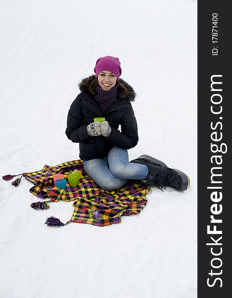 The young woman the brunette sits on a checkered plaid on snow with a mug