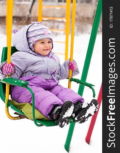 Beautiful girl sitting on a swing outdoor in snow in winter