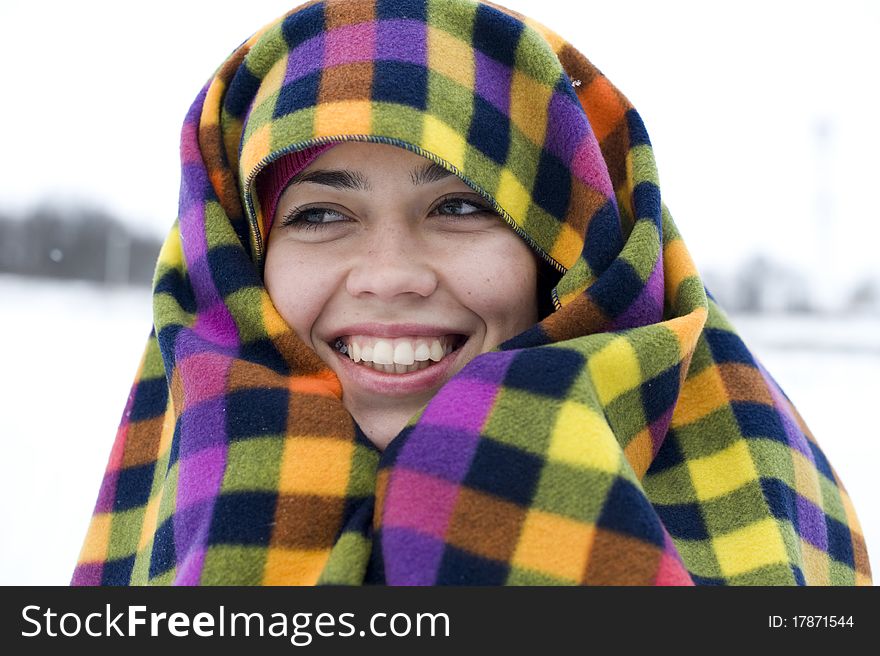 The young woman has muffled in a multi-colored plaid and smiles